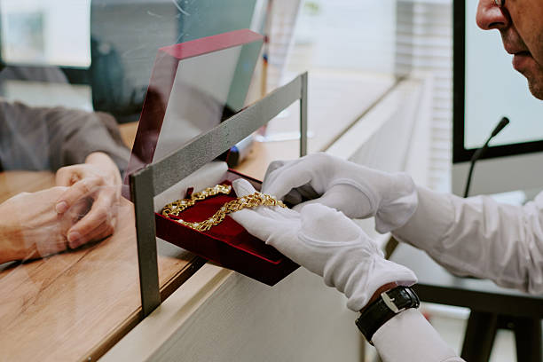 Gloved hand carefully presenting detailed gold jewelry in red velvet box through glass partition, emphasizing luxury and value of piece